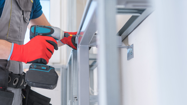 A man is using a cordless drill on a metal structure.