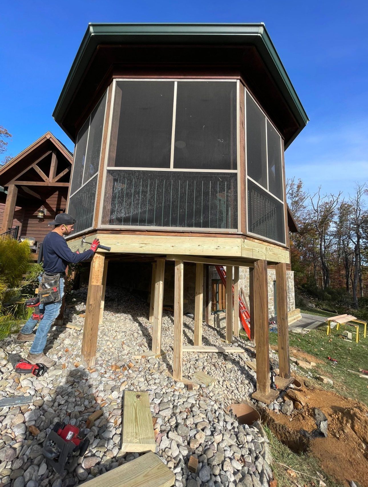 A man is working on a screened in porch in front of a house.