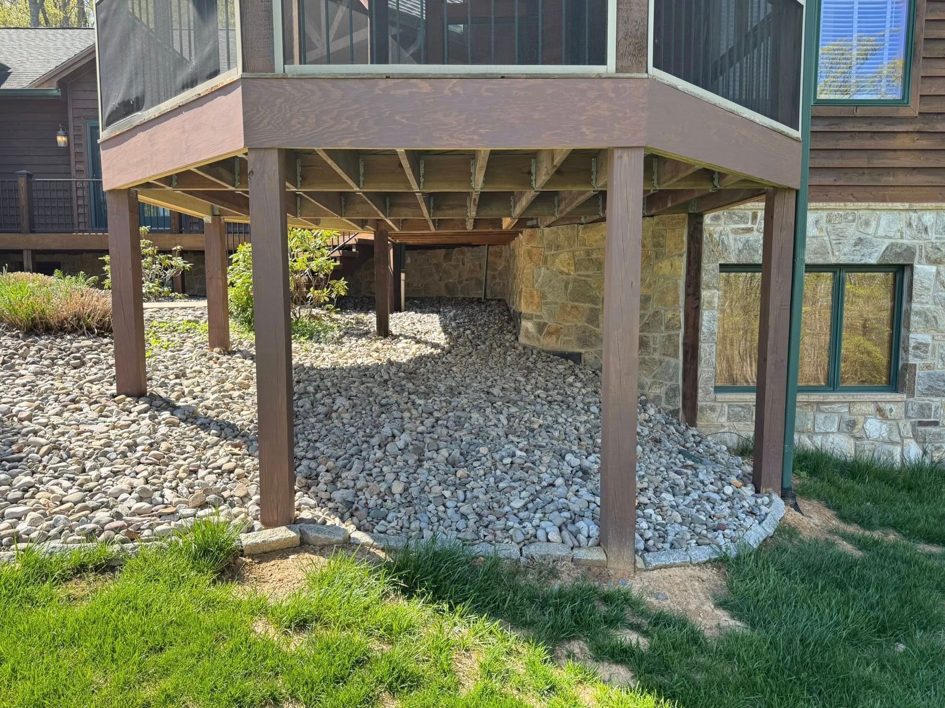 A deck with a screened in area underneath it is sitting next to a house.