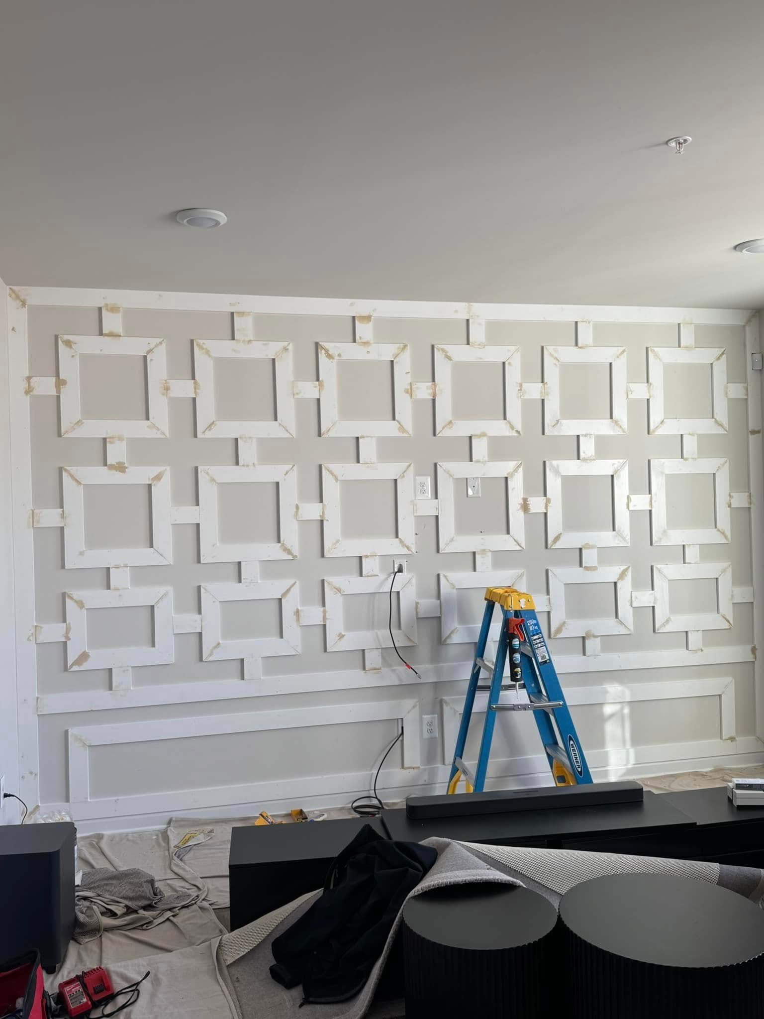 A living room with a ladder in front of a wall with squares on it.