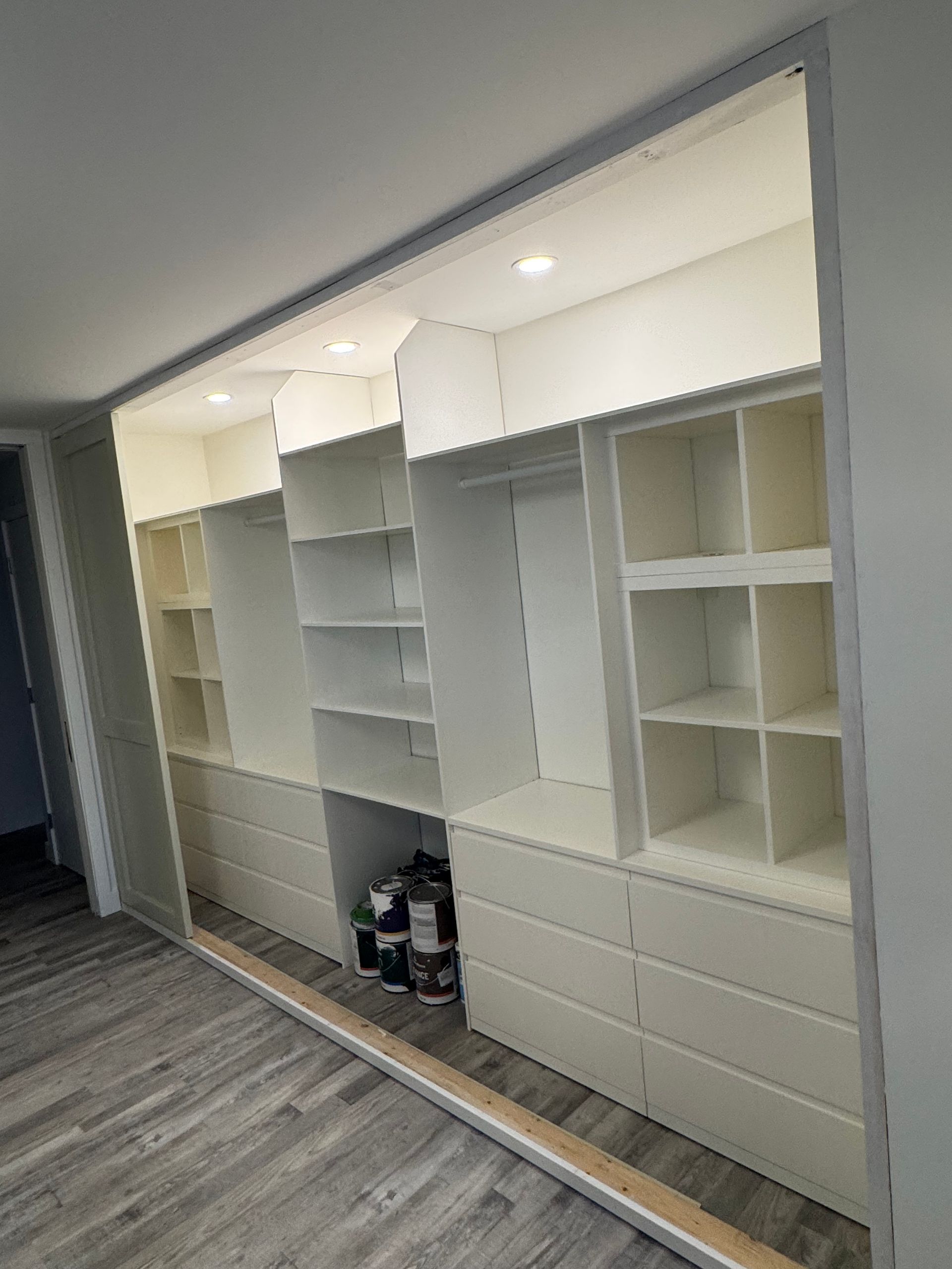 Built-in white shelving and cabinets along a wall in a modern room with gray wood flooring.