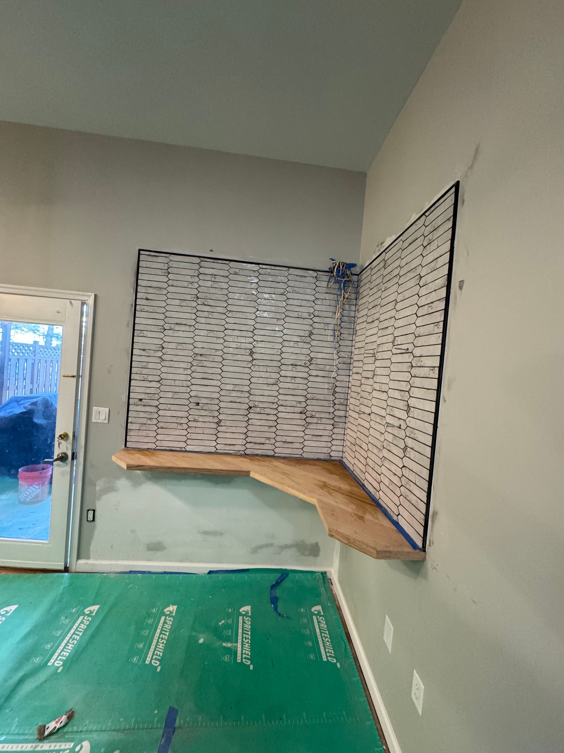 Partially renovated room with exposed wall tile, wooden counter, and green floor covering