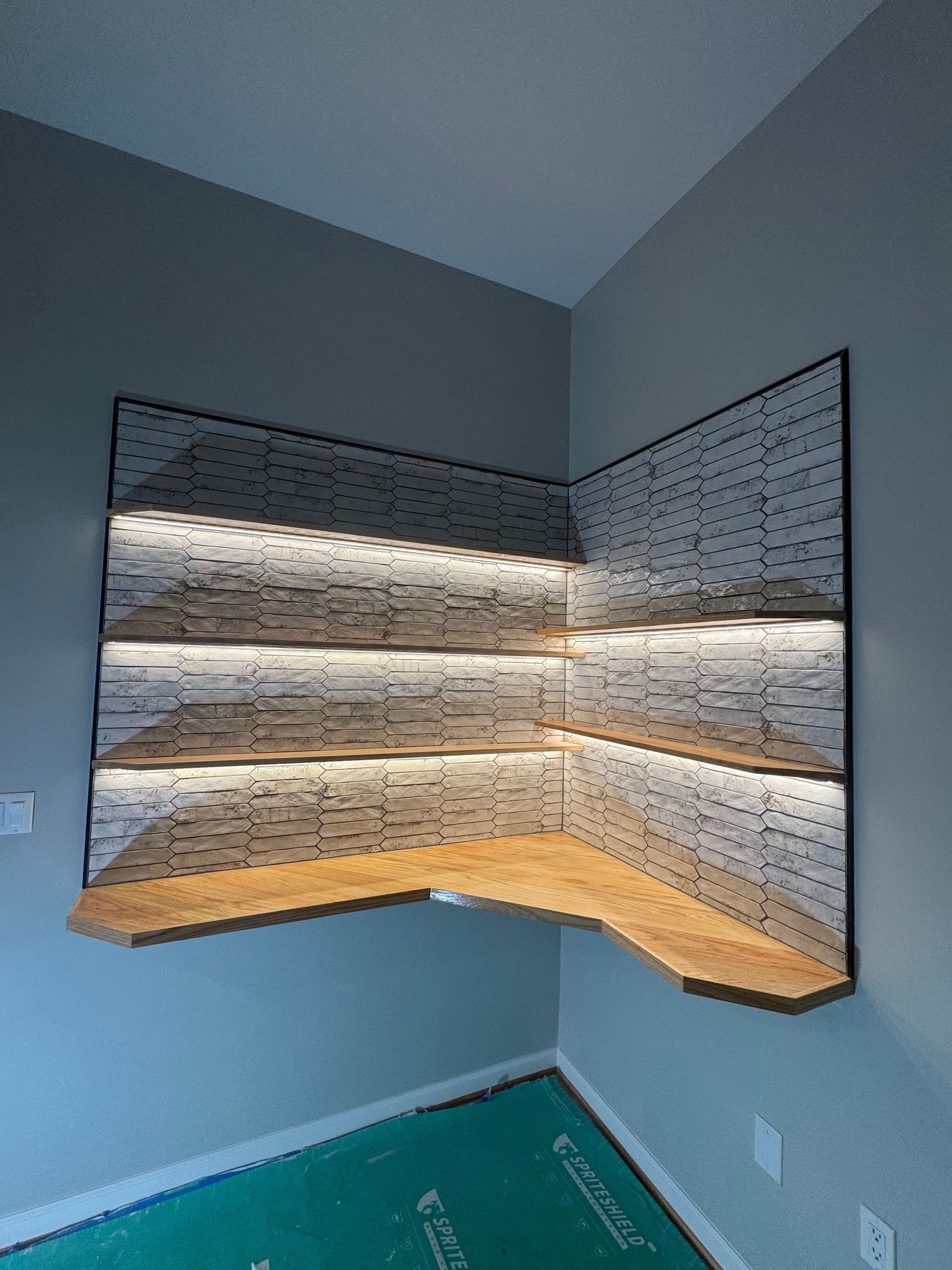 Built-in corner desk with wood top, patterned wallpaper, and LED lighting in a small room.