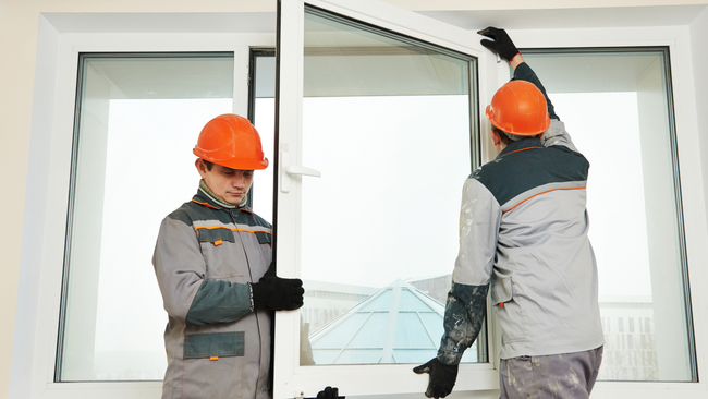 Two men are installing a window in a house.