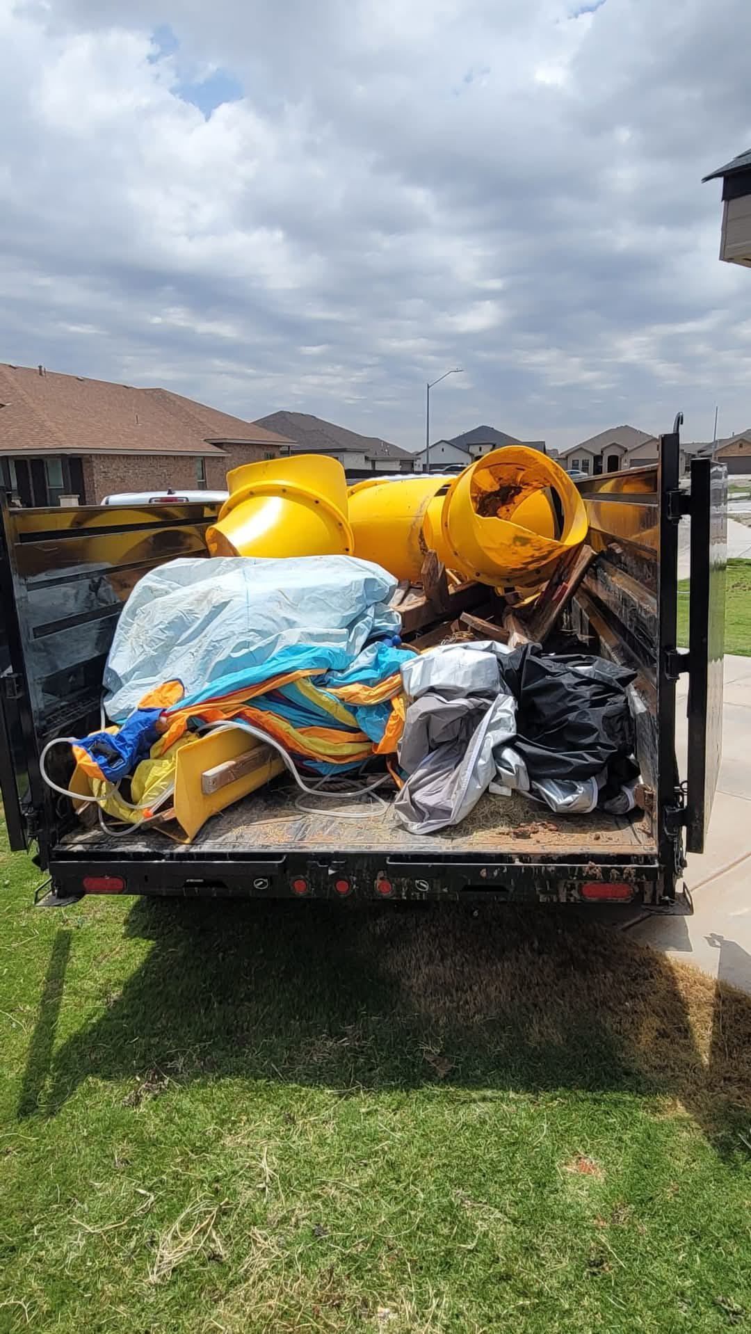 A dumpster filled with junk is parked in the grass.