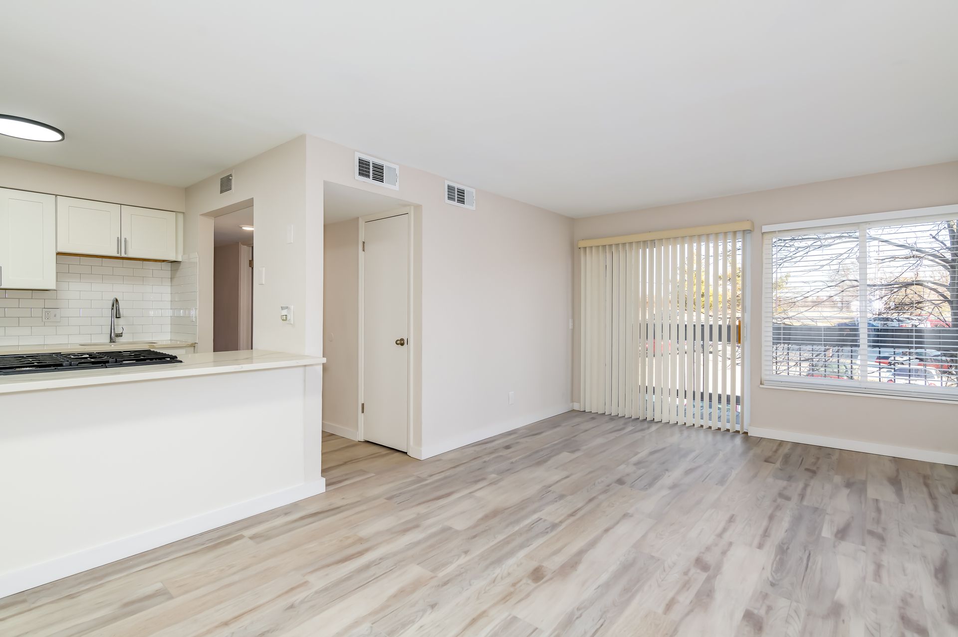 A living room with hardwood floors and a kitchen in the background.