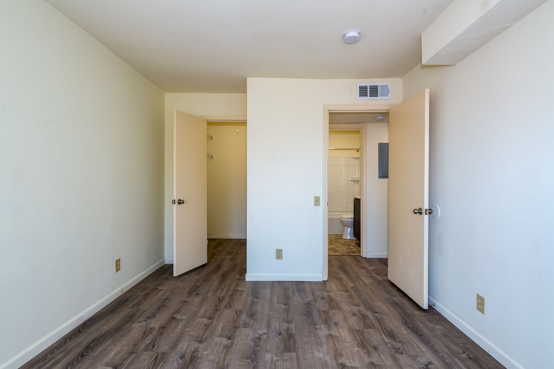 An empty bedroom with hardwood floors and white walls.