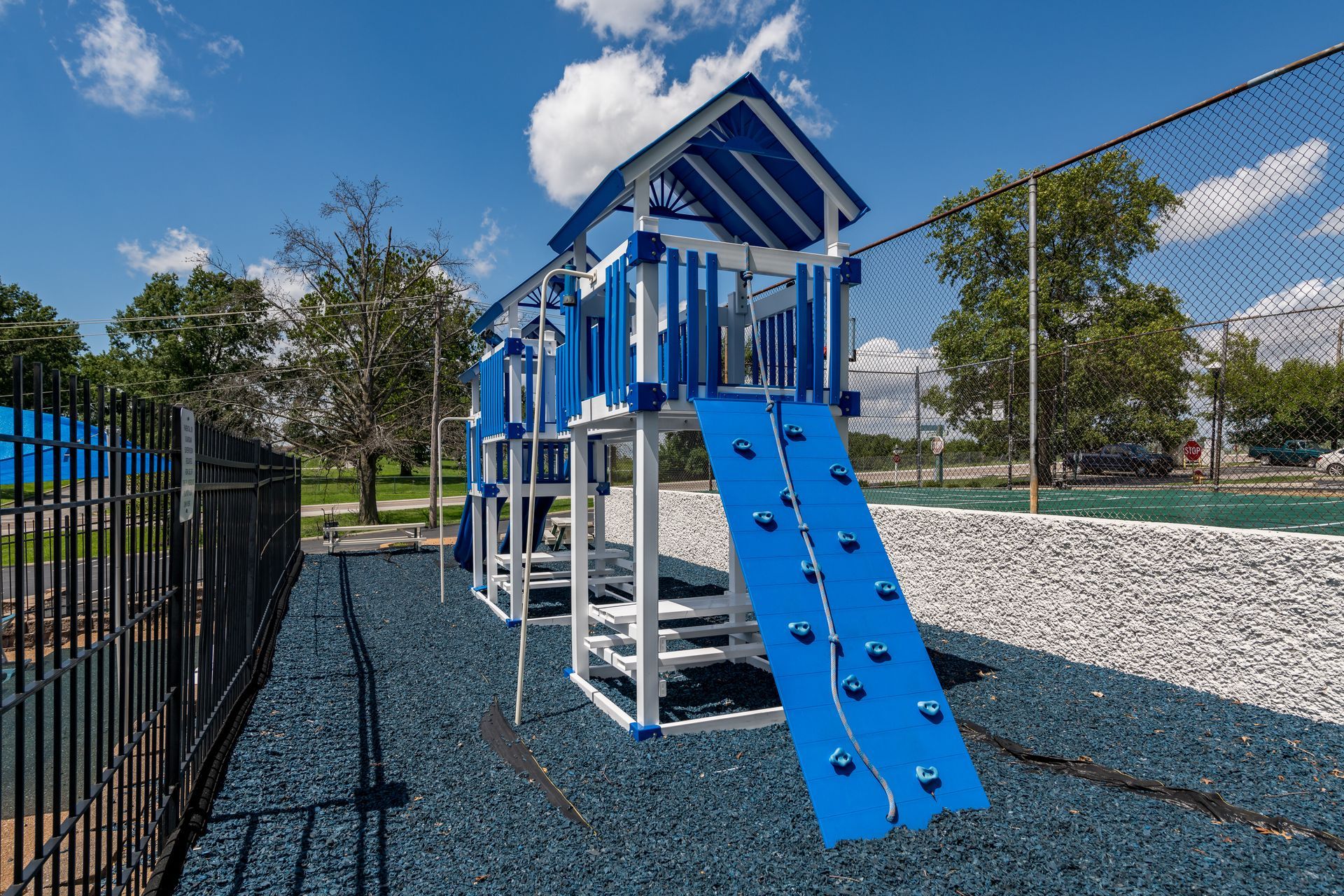 A blue and white playground set in a park with a fence in the background.