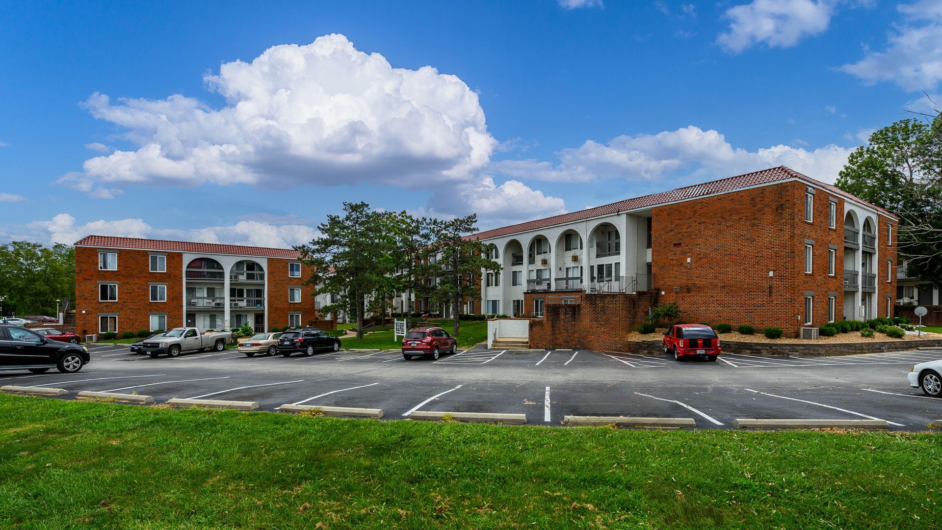 A large apartment building with a lot of cars parked in front of it.