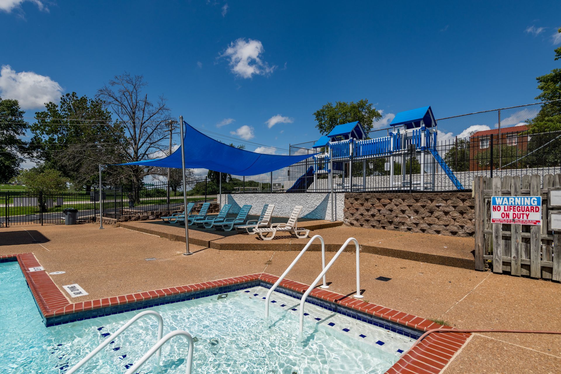 A swimming pool with stairs and a playground in the background.
