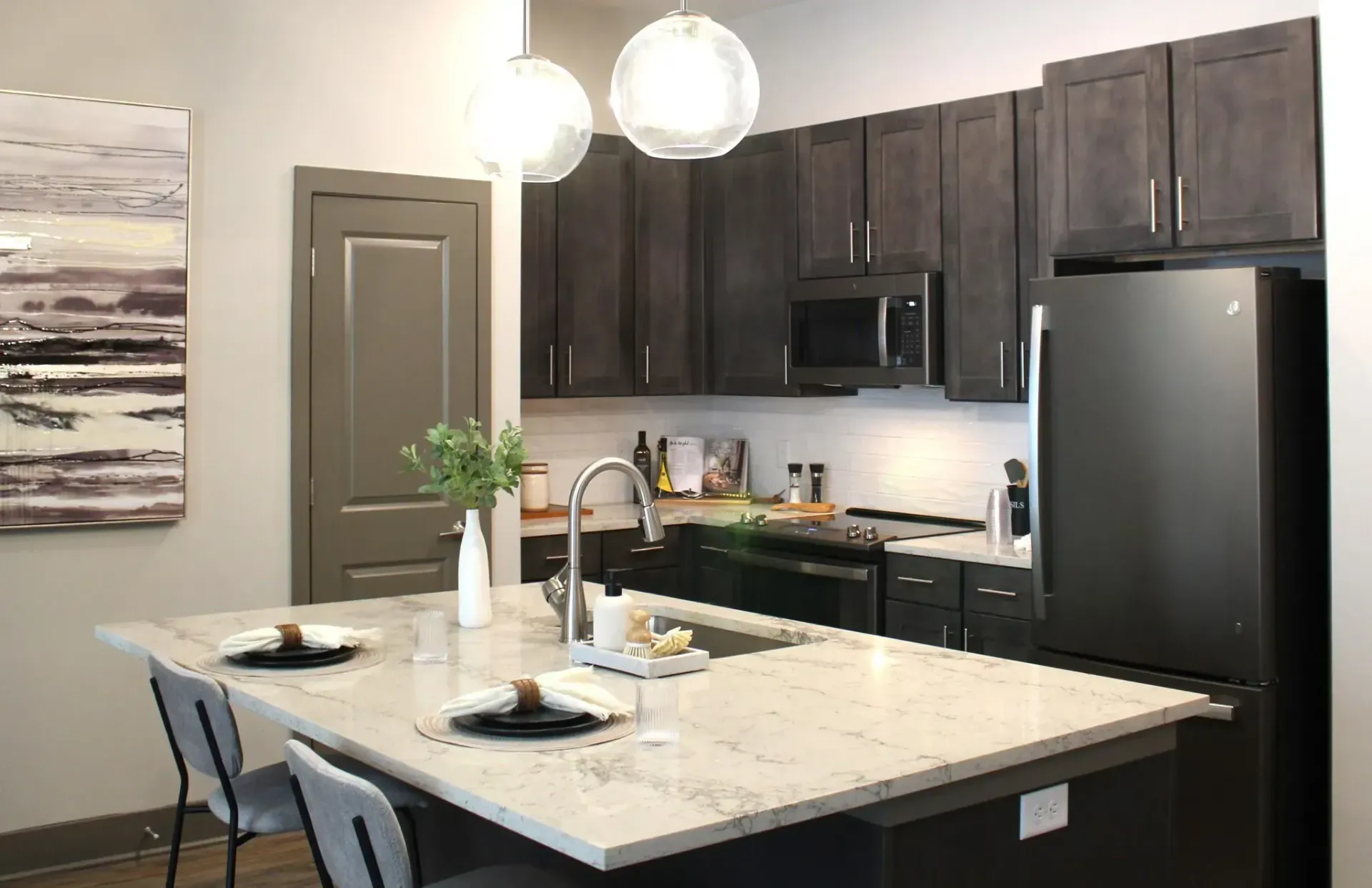 Modern apartment kitchen with dark cabinets, marble island, and stainless appliances.