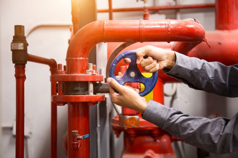 A Man Is Fixing A Valve On A Red Pipe — BAS Plumbing & Drainage In Forresters Beach, NSW