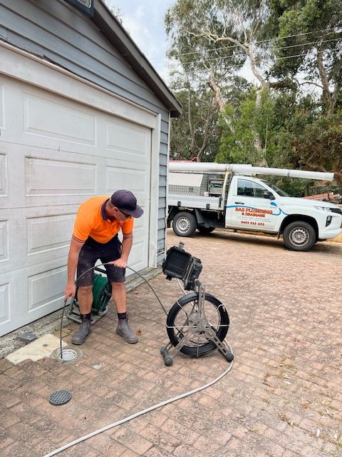 A Plumber Is Fixing A Blocked Drain On A Driveway — BAS Plumbing & Drainage In Forresters Beach, NSW
