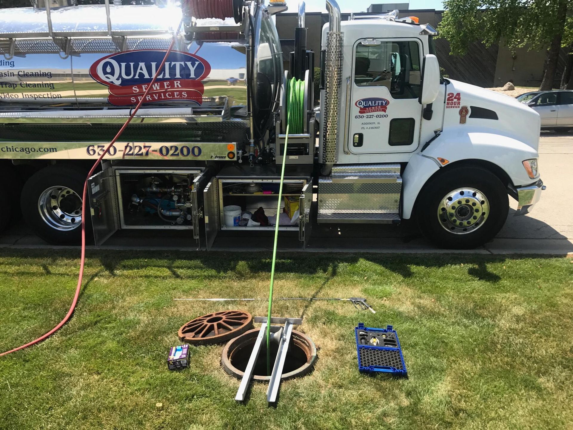 A white truck with a hose attached to it is parked in the grass.