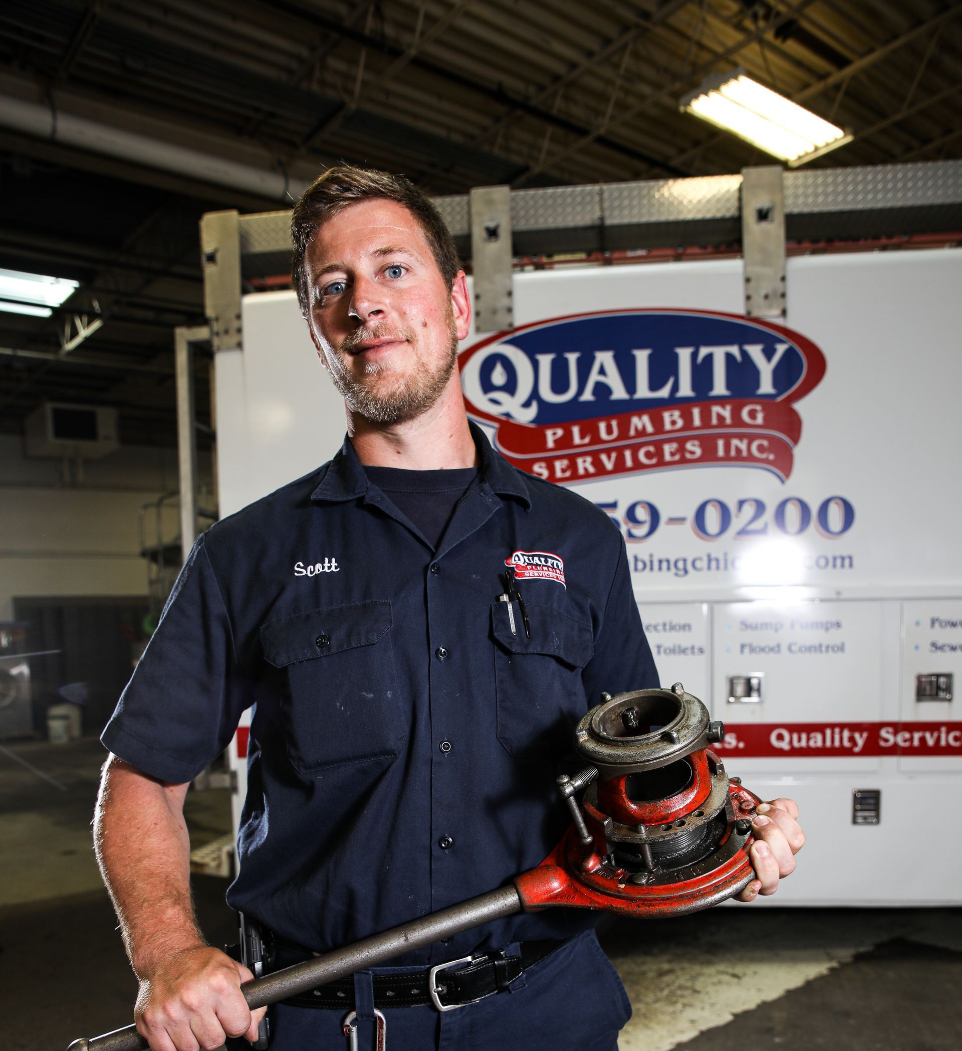 A plumber from Quality Plumbing Services Inc. is holding a pipe wrench in front of a quality plumbing service truck