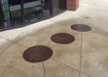 Three manhole covers are on the sidewalk in front of a building.