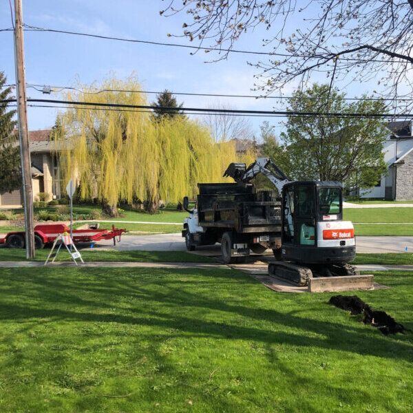 A bobcat excavator is parked next to a dump truck for sewer repair in Bloomingdale, IL