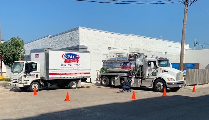 Two trucks are parked in front of the Quality Plumbing Services, Inc building.