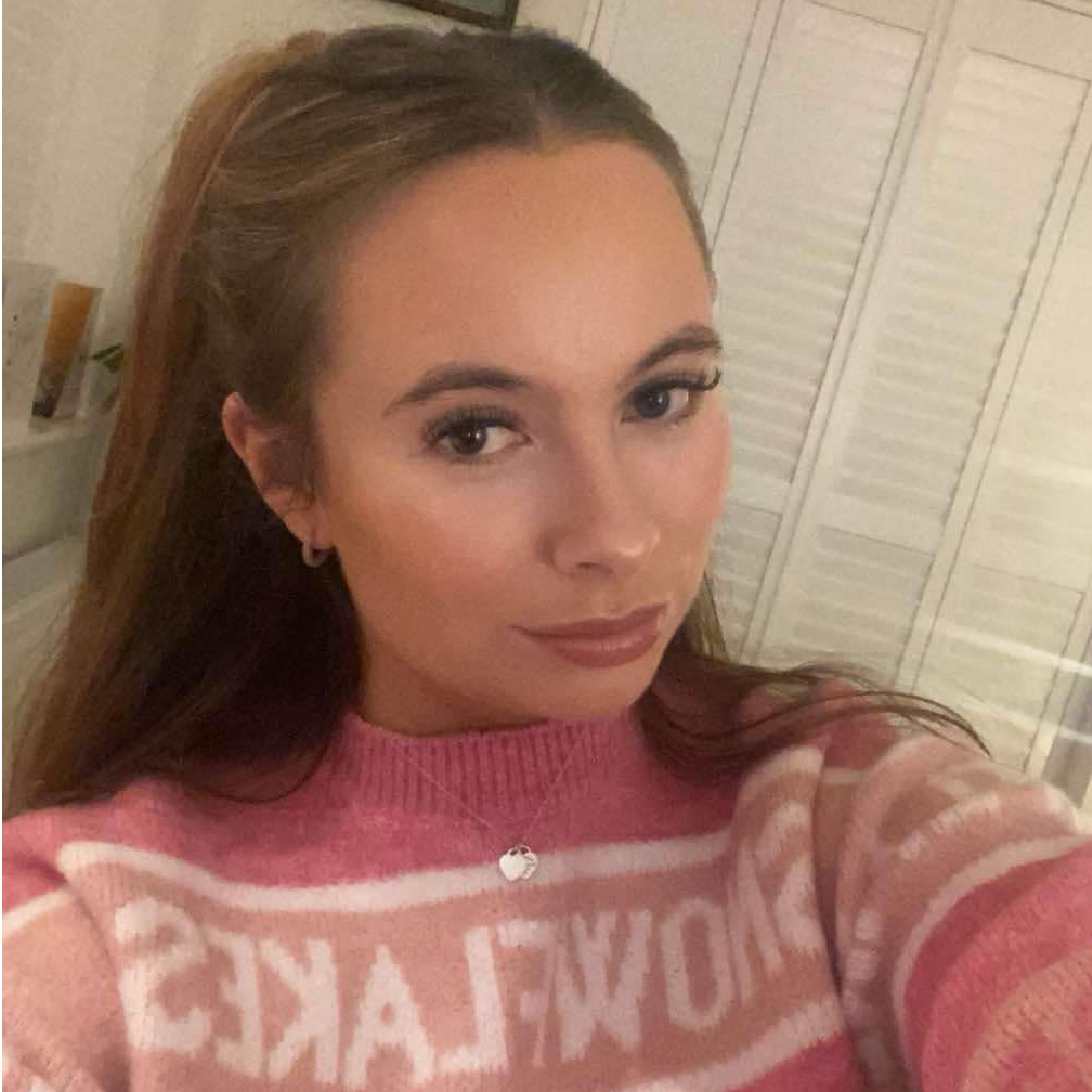 A woman in a pink sweater is taking a selfie.
