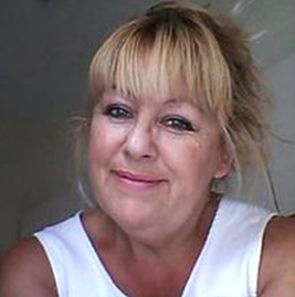 A woman with blonde hair is wearing a white tank top and smiling.