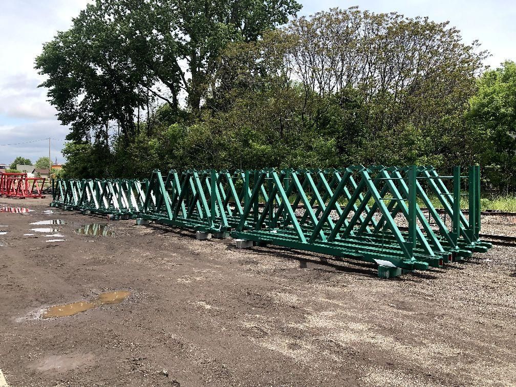 A row of green metal structures are sitting on top of a dirt field.