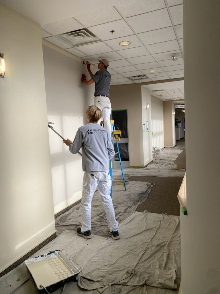 Two men are painting a wall in a hallway.