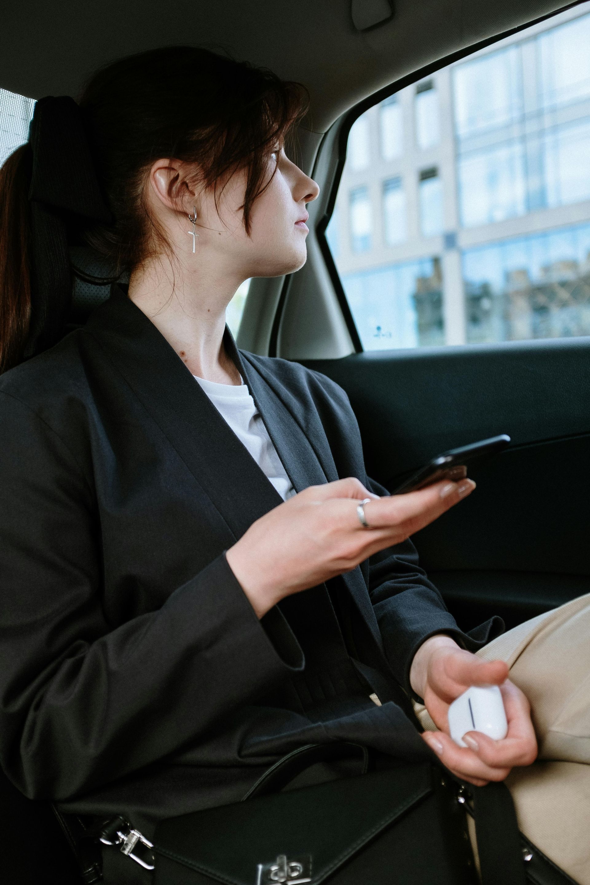 A woman is sitting in the back seat of a car holding a cell phone.