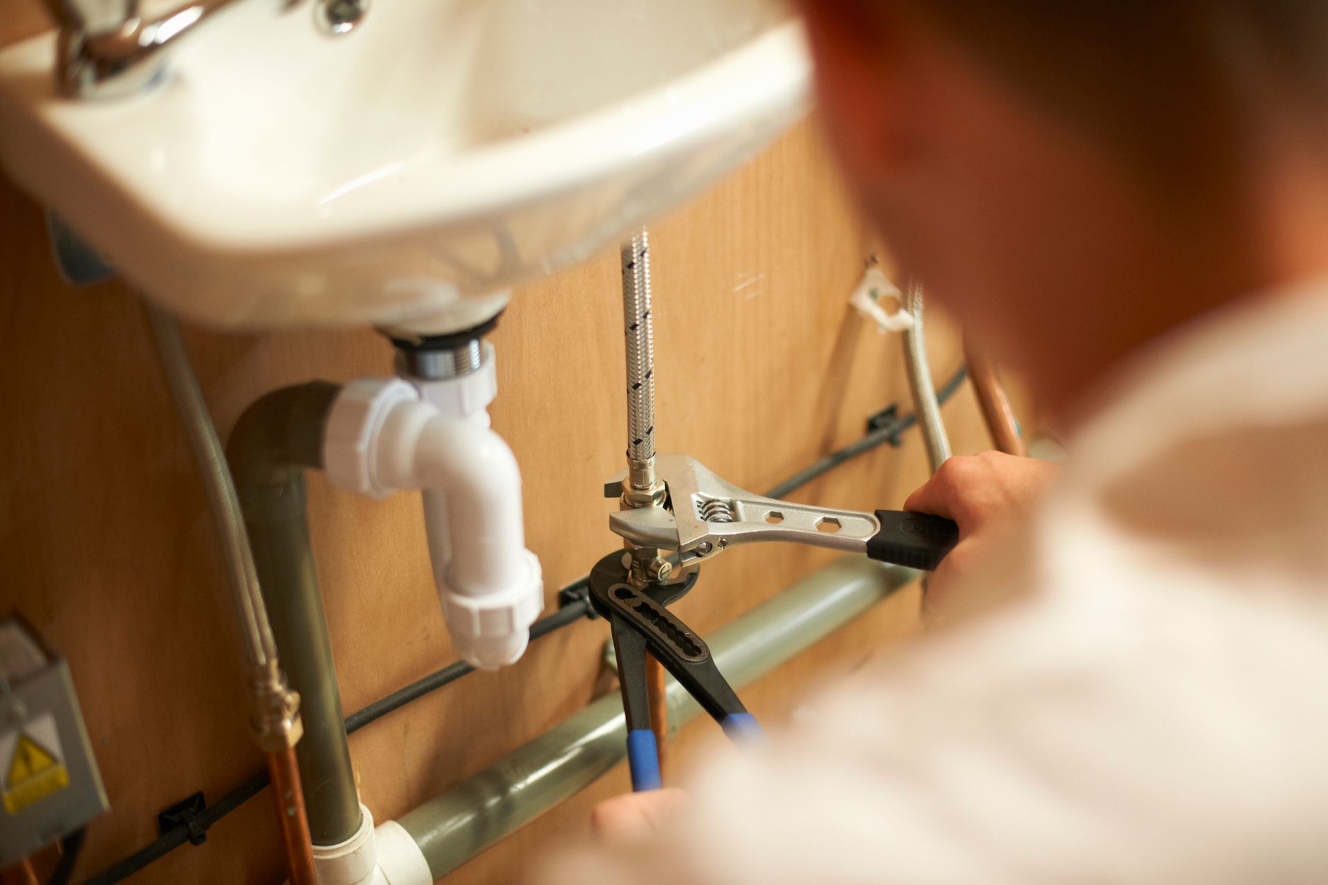 A man is fixing a sink with a wrench.