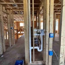 Construction site showing wooden wall framing, a white PVC drain pipe, a recessed laundry box, and blue electrical boxes.