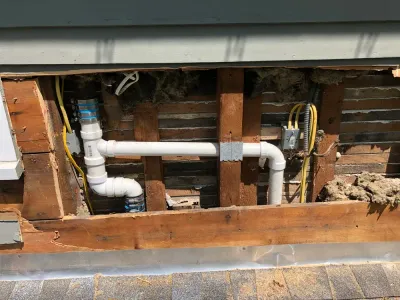 A wall section with exposed wood framing, electrical wiring, and white PVC plumbing pipes.