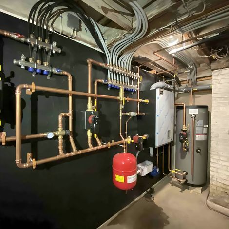 Mechanical room featuring a boiler, copper piping manifolds, a red expansion tank, and a hot water heater on a black wall.