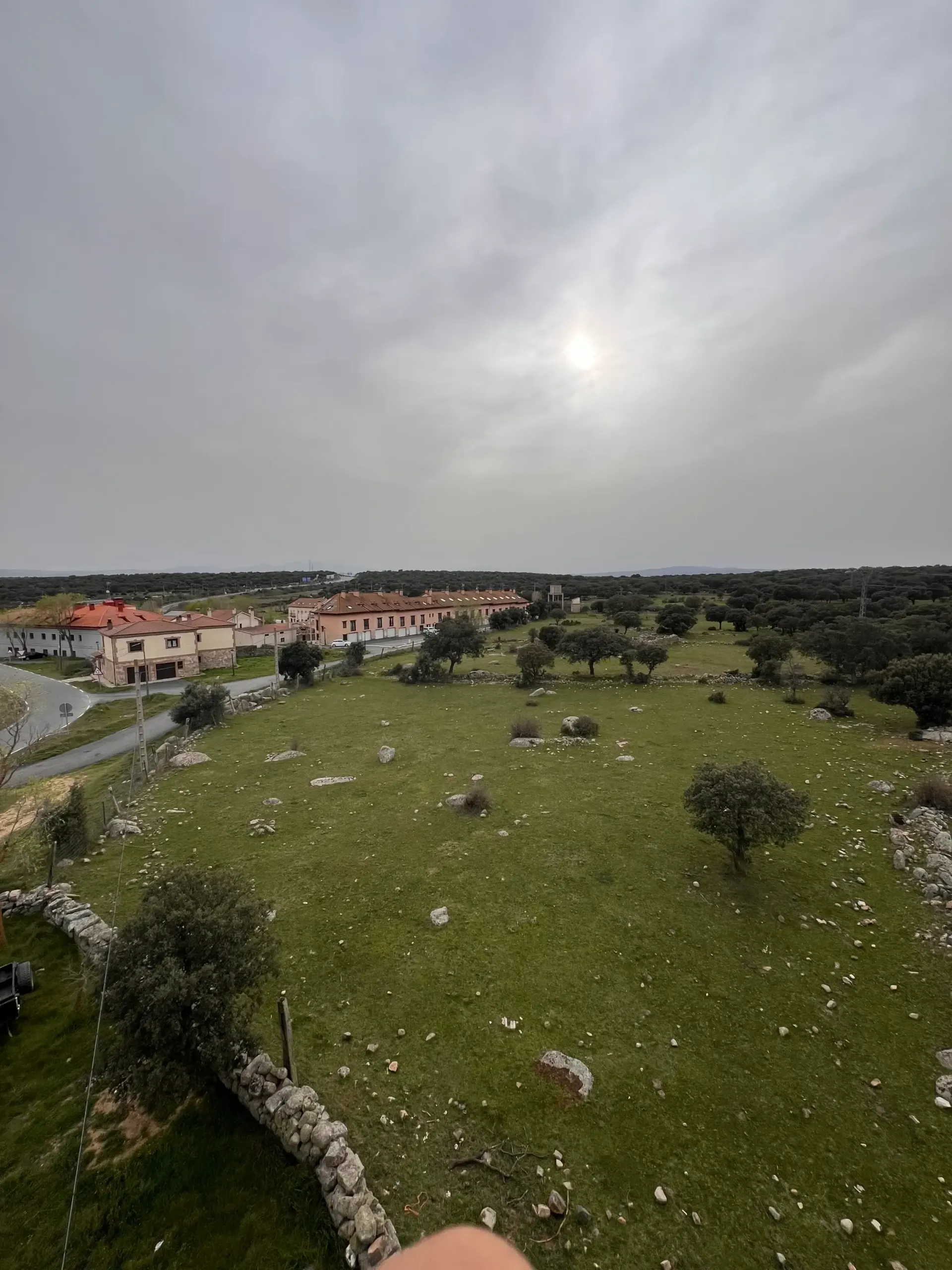 Ladera cubierta de hierba con rocas dispersas que domina un pueblo bajo un cielo nublado.