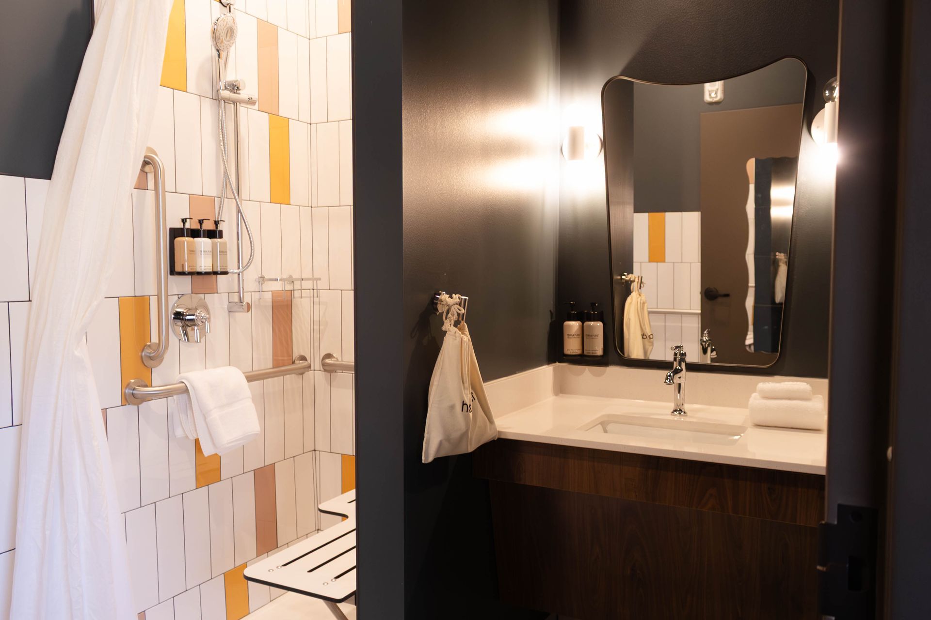 A bathroom featuring a shower with a white curtain, tiled walls, and a separate vanity area with a dark cabinet and mirror.