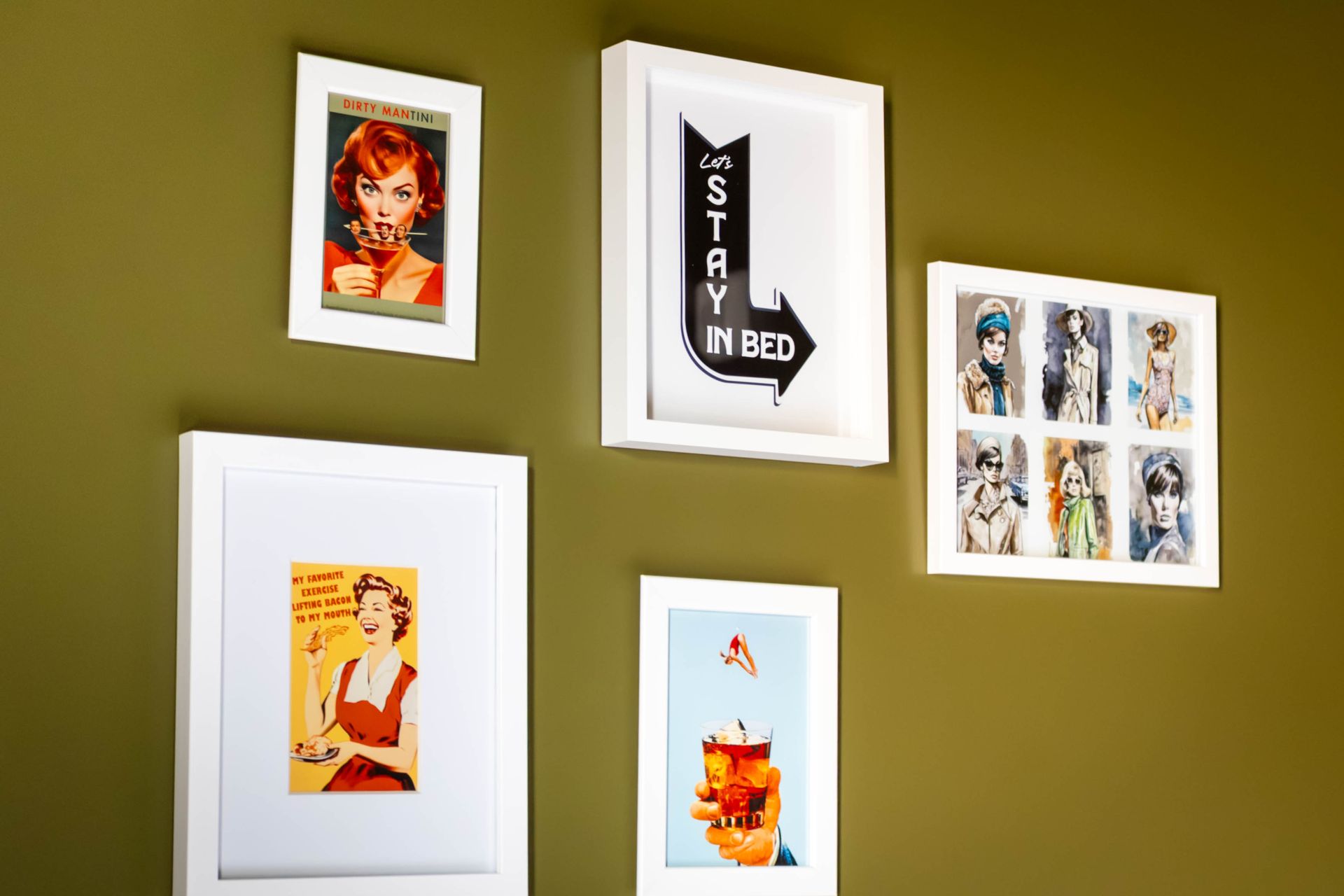 A gallery wall of five white-framed prints, featuring vintage-style art, against an olive green wall.