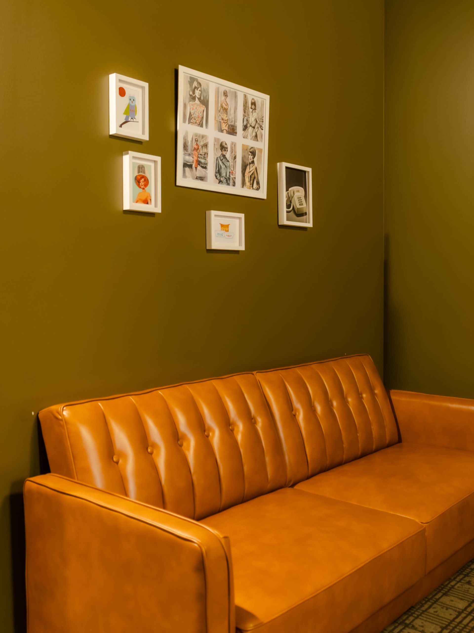 A tan leather couch sits against a dark olive wall adorned with a small gallery of framed art.