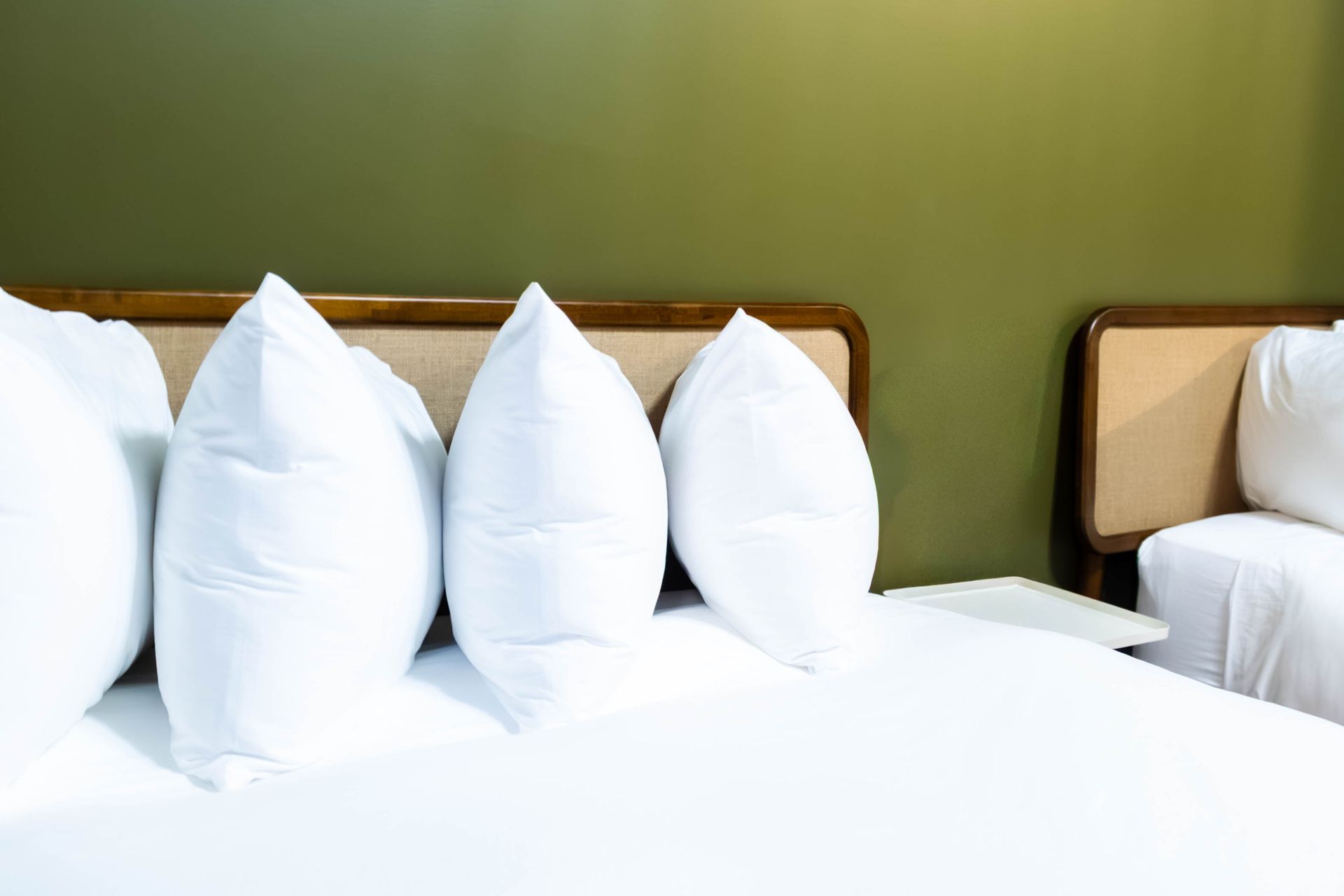 Several fluffy white pillows arranged on a bed against a plain green wall in a hotel room.