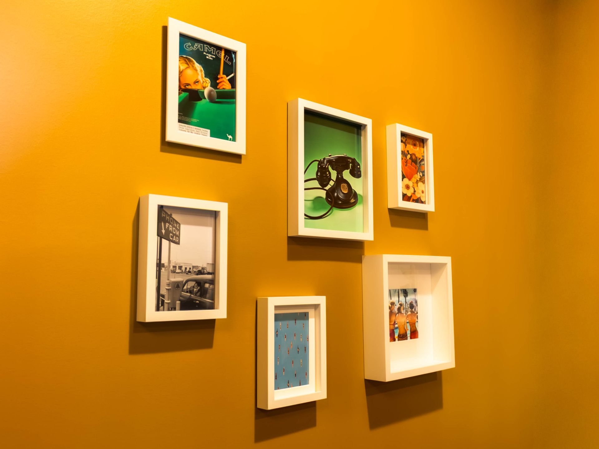 Six assorted framed photographs and prints are arranged on a vibrant yellow wall.