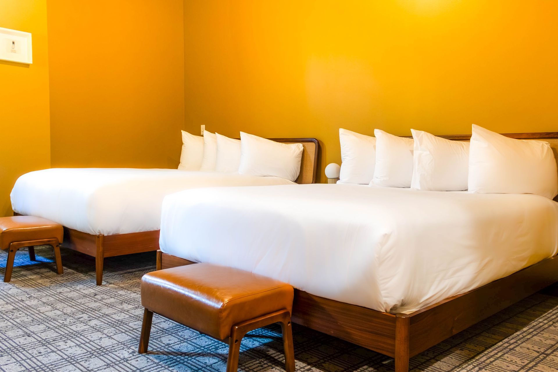 A bedroom featuring two beds with white linens and white pillows, situated against a dark wall with a bedside lamp.