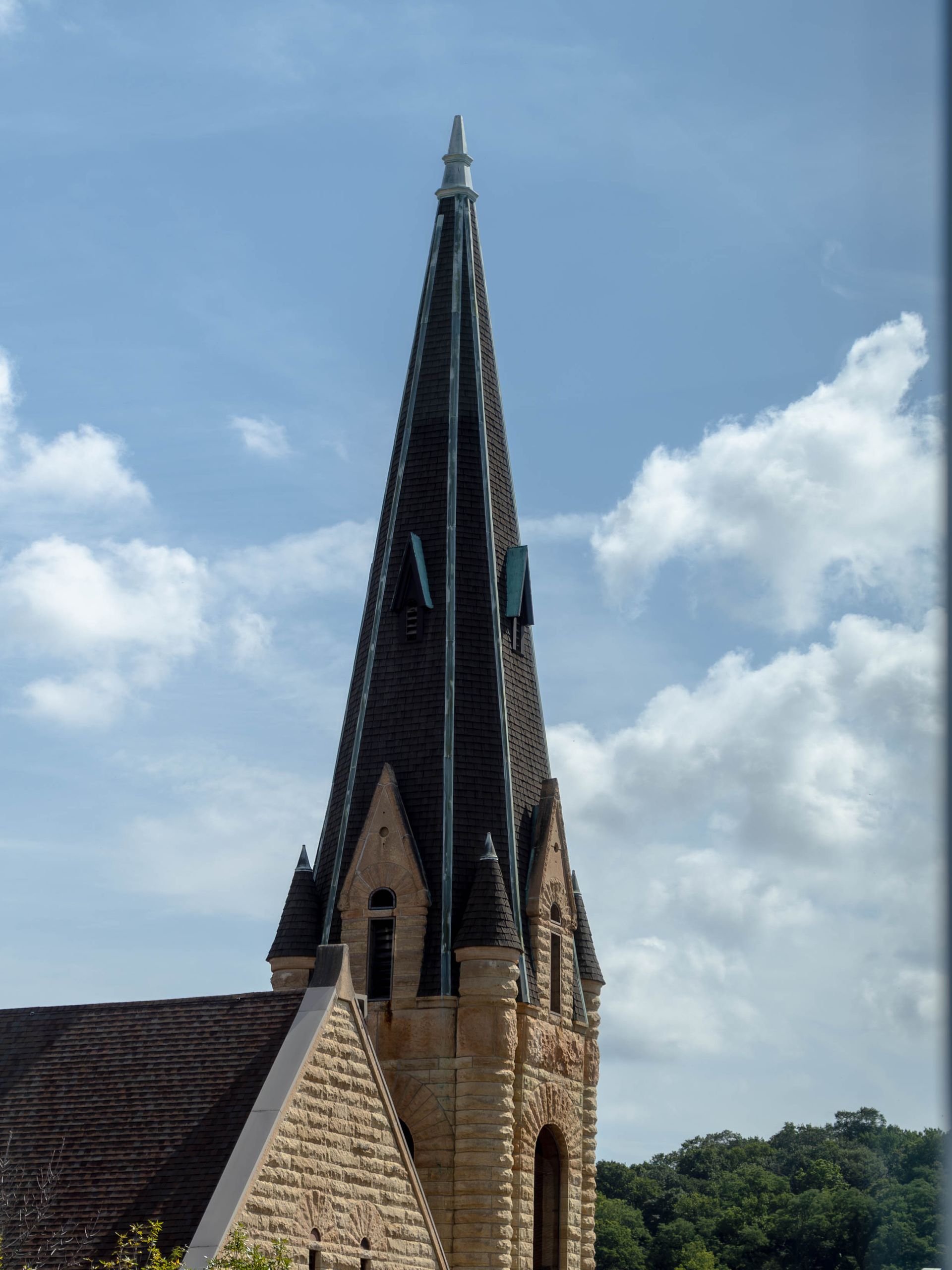 A stone church spire under a blue sky with white clouds.