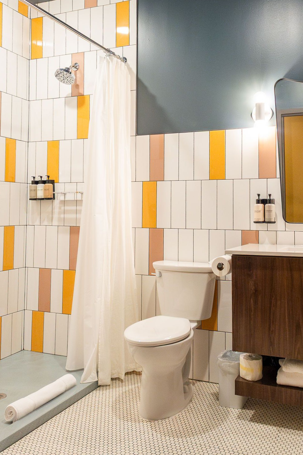 A bathroom with white, yellow, and tan vertical-patterned wall tiles, a white shower curtain, and a modern wooden vanity.