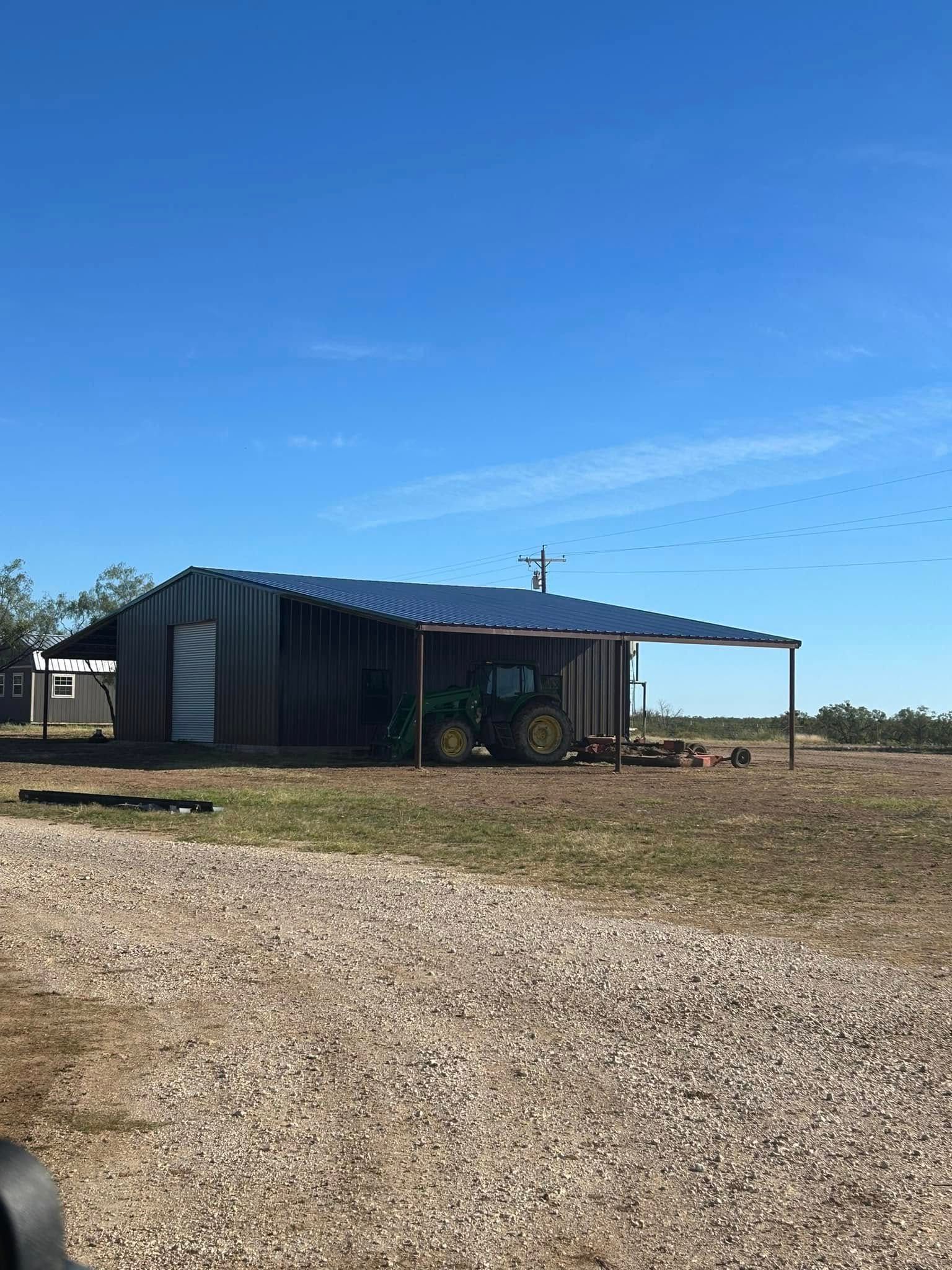 A tractor is parked under a shed in a field.