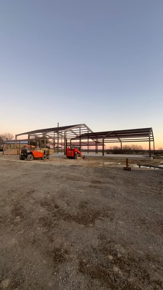 A large metal structure is being built in a gravel lot.