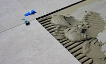 Tile installation: gray tile, mortar, notched trowel, blue leveling clips.