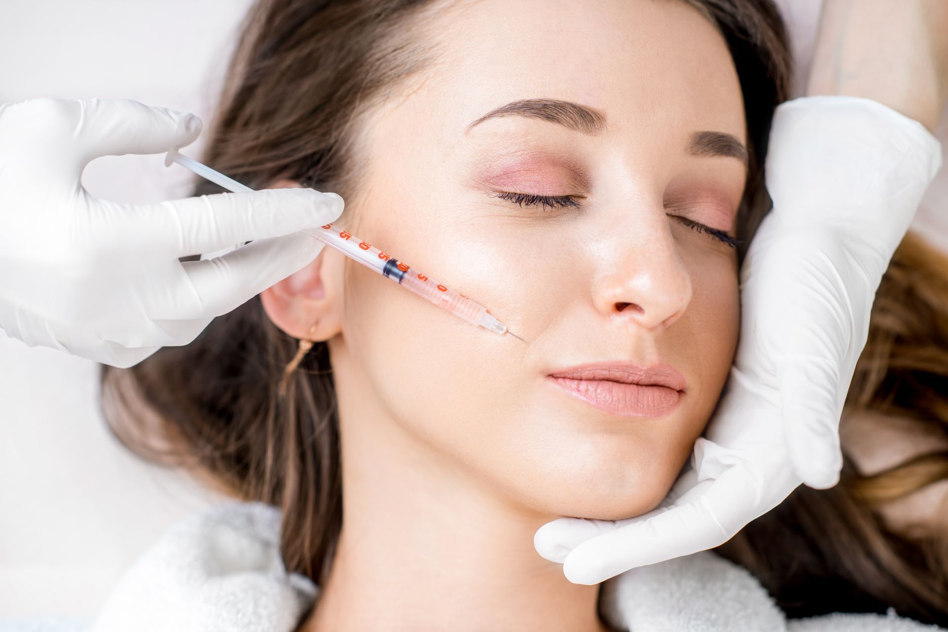 A woman receiving a Botox injection in the lip zone, lying on a medical couch