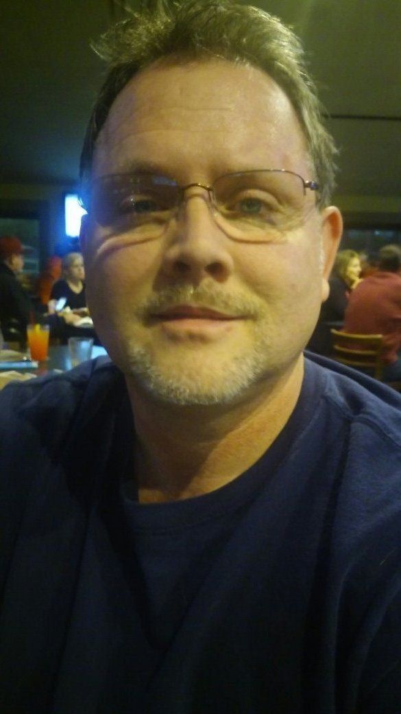 A man with glasses and a beard is sitting at a table in a restaurant.