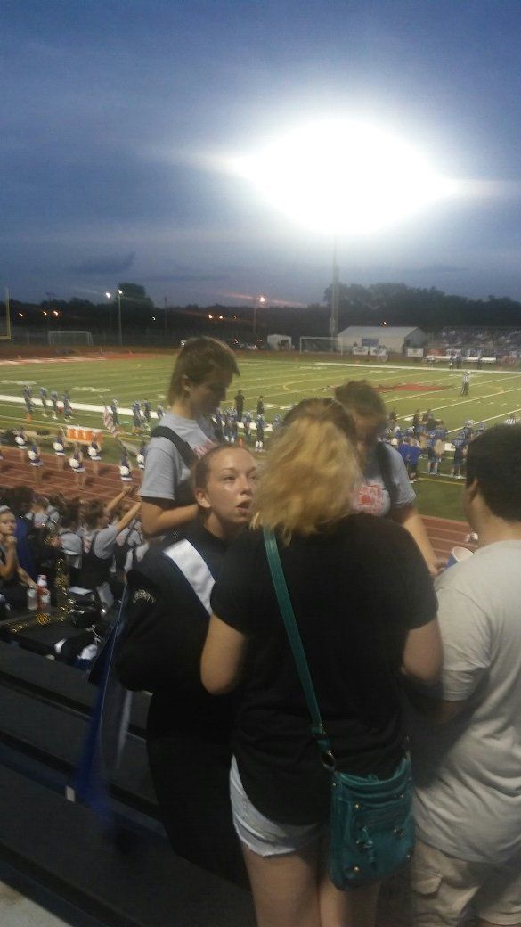 A group of people are standing in the stands at a football game.