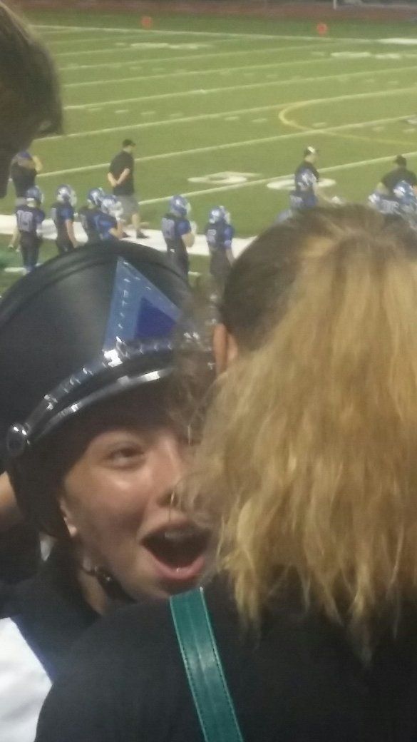 A woman wearing a police hat is talking to another woman on a football field.