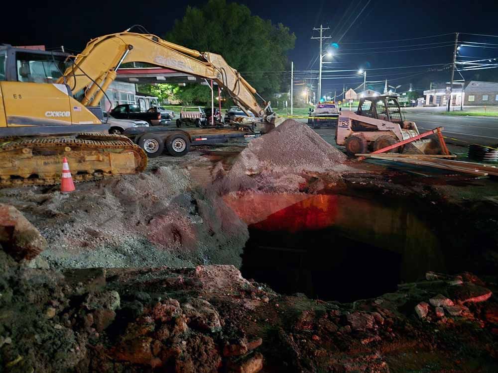 A yellow excavator is digging a hole in the ground at night.