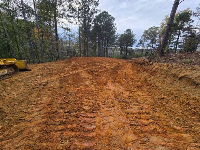 A bulldozer is driving down a dirt road in the woods.