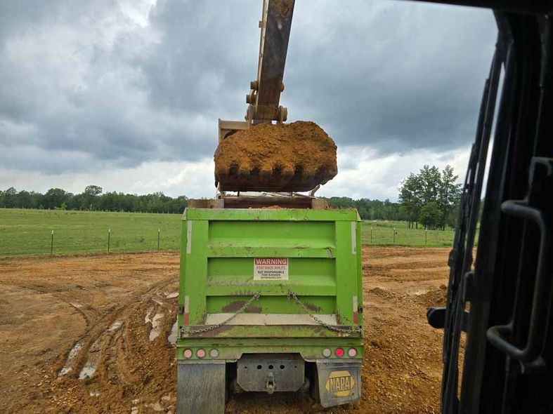 A green dump truck is being loaded with dirt by an excavator.